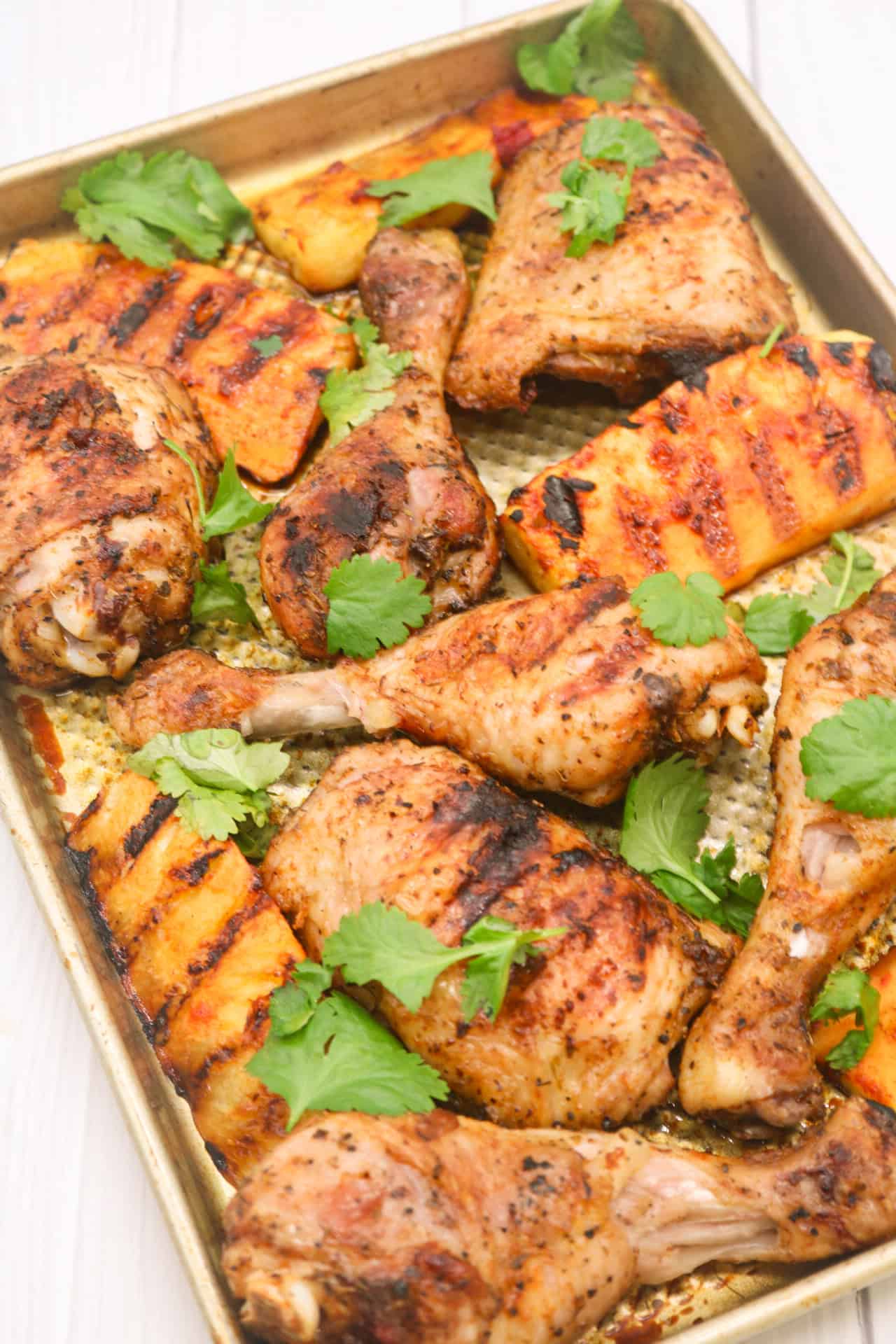 Cajun chicken with charred pineapple wedges on a large baking tray, garnished with coriander.