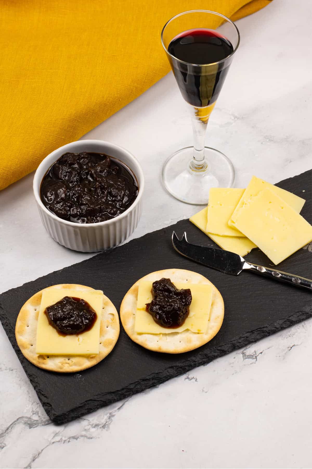 Caramelised red onion chutney made in the Thermomix in a white ramekin with crackers, cheese and chutney on a black slate, and a glass of port on the side.