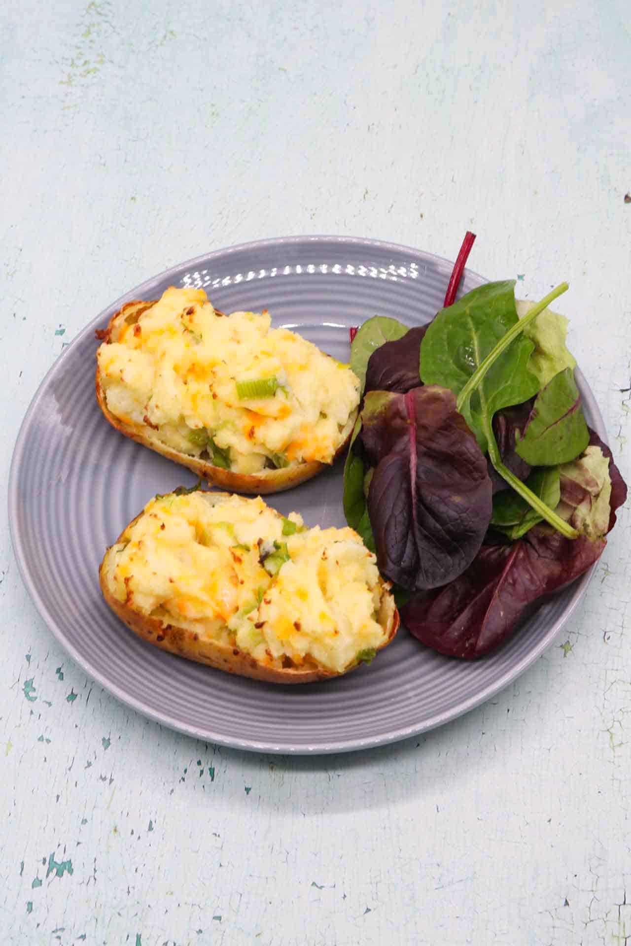 Cheese and spring onion baked potato on grey plate with salad leaves