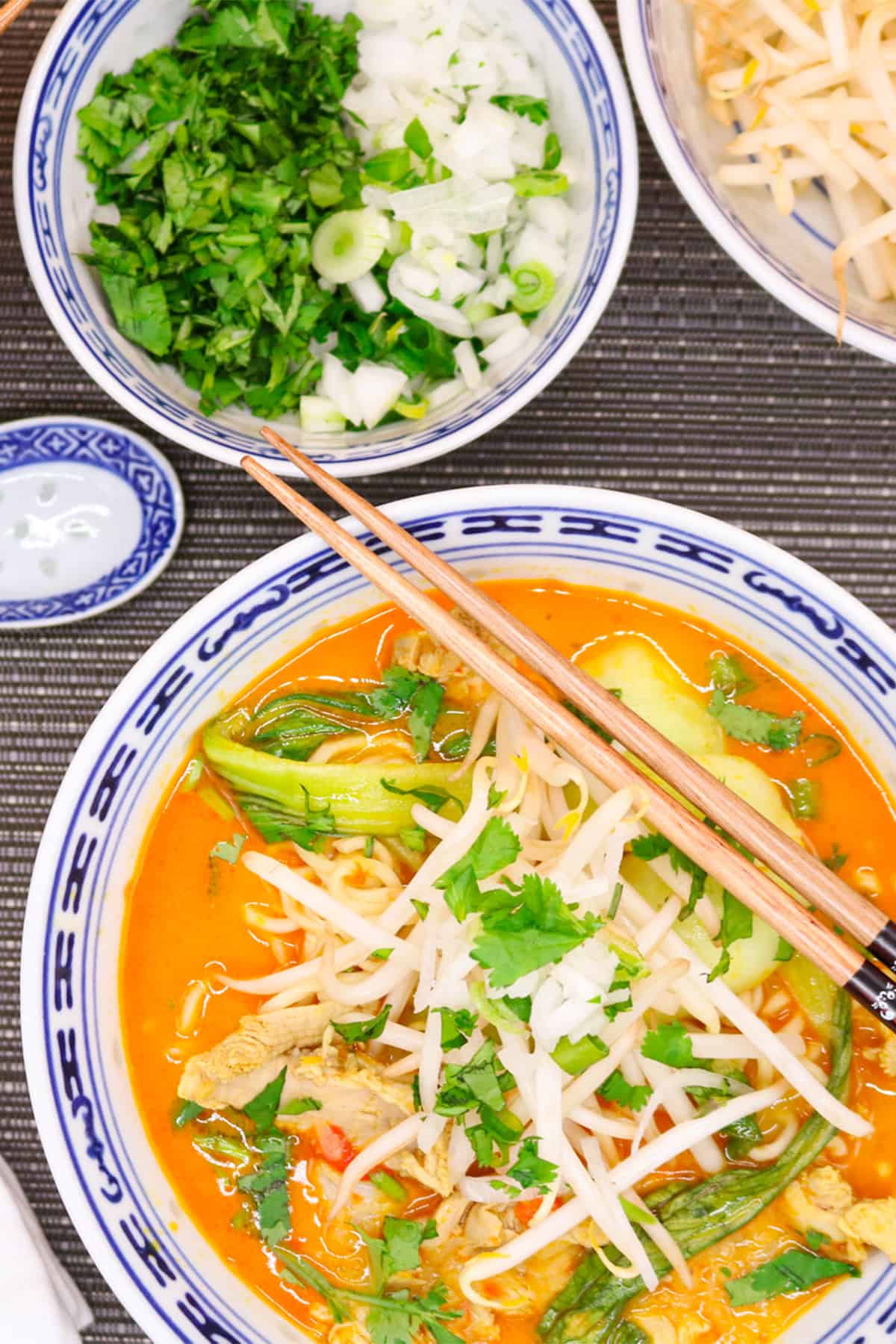 Chiang mai noodles made in the Thermomix in an oriental bowl with chopsticks and bowls of beansprouts, coriander and spring onions in the background.