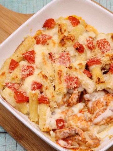 Chicken pasta bake in a white square oven dish sitting on a wooden board.