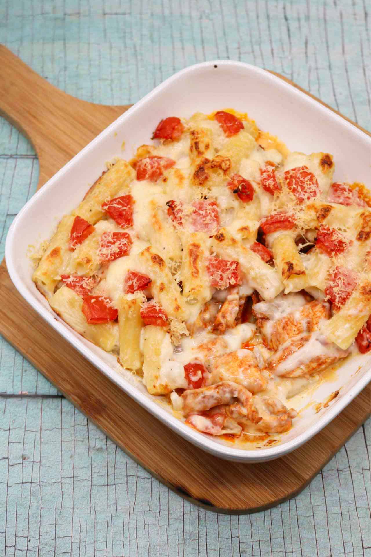 Chicken pasta bake in a white square oven dish sitting on a wooden board.