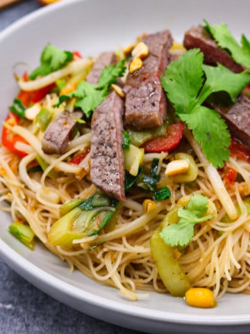 Chilli beef and vegetable rice noodles with peanuts in a grey bowl.