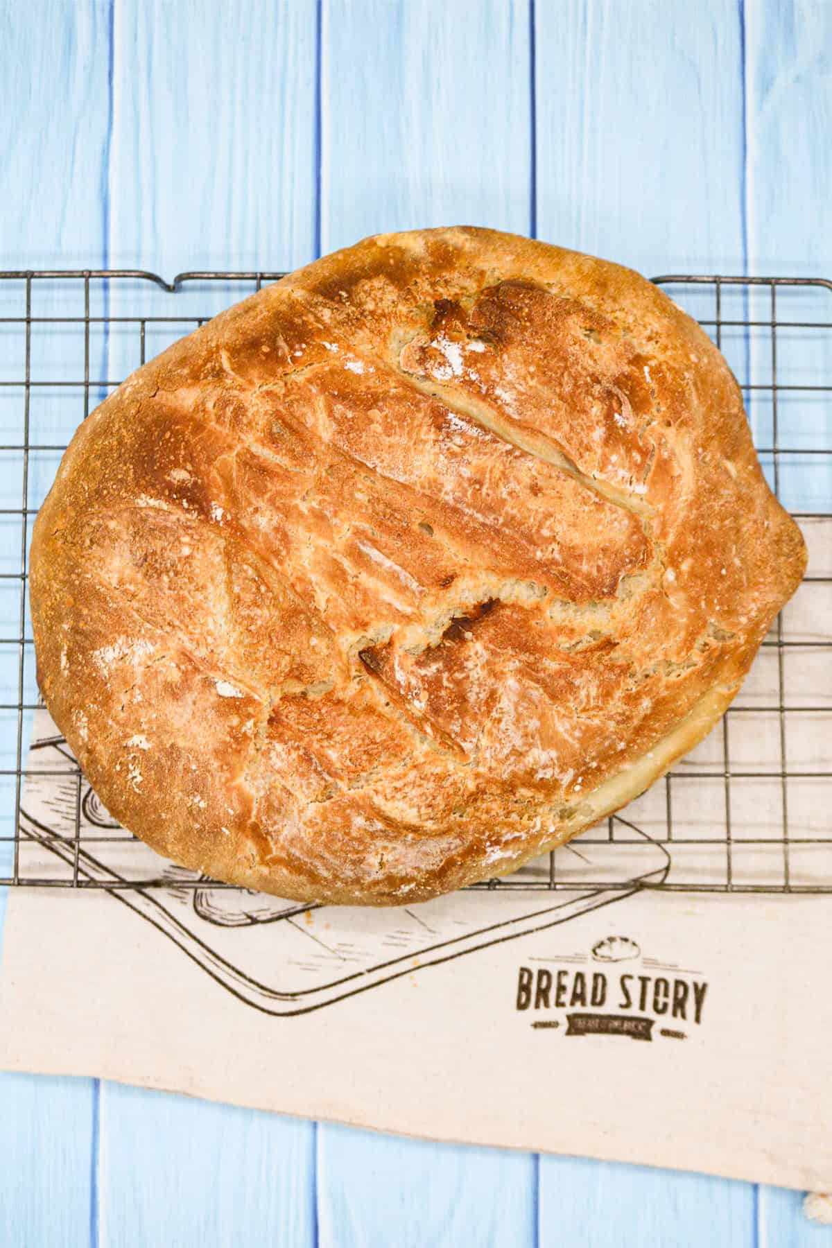 Crusty bread on a cooling rack sitting on top of a cloth bread bag.