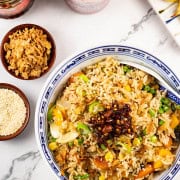 Easy vegetable fried rice in a blue and white oriental serving bowl with spoon and Asian condiments on the side.