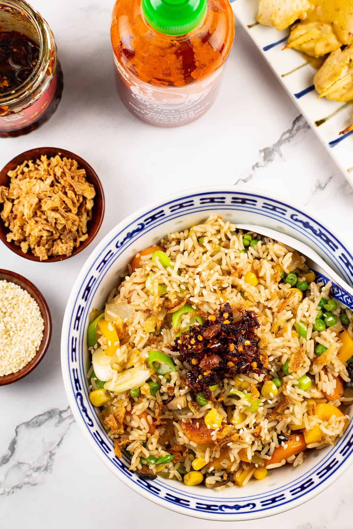 Easy vegetable fried rice in a blue and white oriental serving bowl with spoon and Asian condiments on the side.