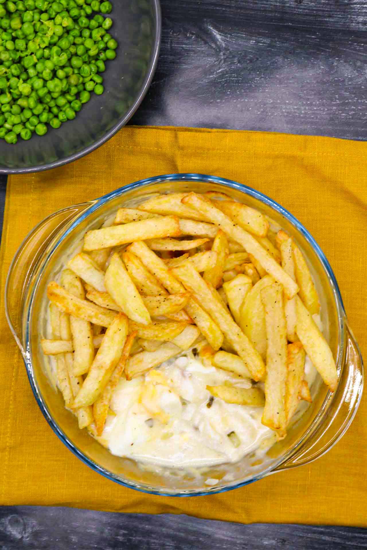 Fish and chip pie in a round glass serving bowl plus a bowl of peas on the side