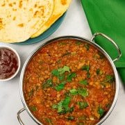 Green lentil dal in a balti dish with a plate of quick naan breads and small dish of mango chutney on the side.