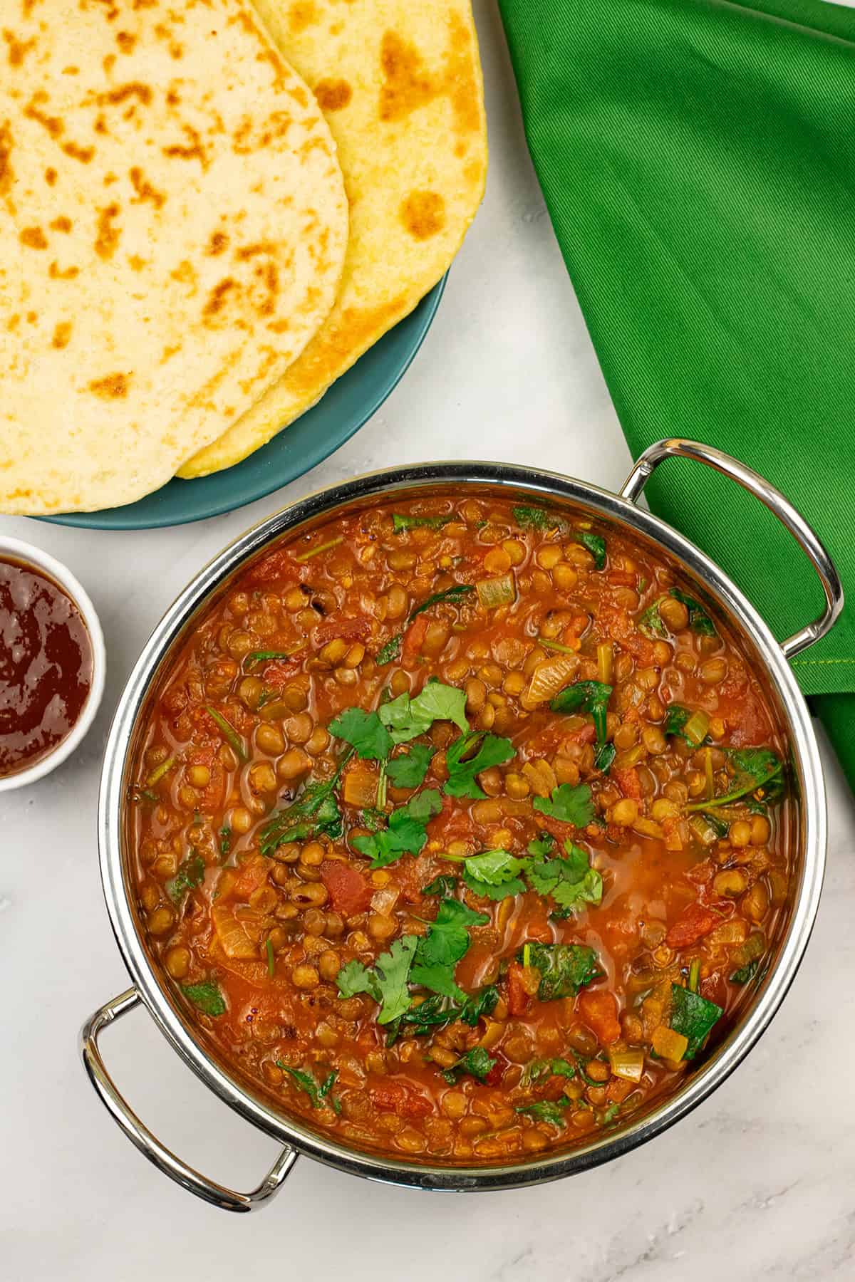Green lentil dal in a balti dish with a plate of quick naan breads and small dish of mango chutney on the side.