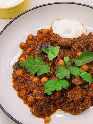 Harissa beef stew in a bowl garnished with coriander and sour cream on the side.