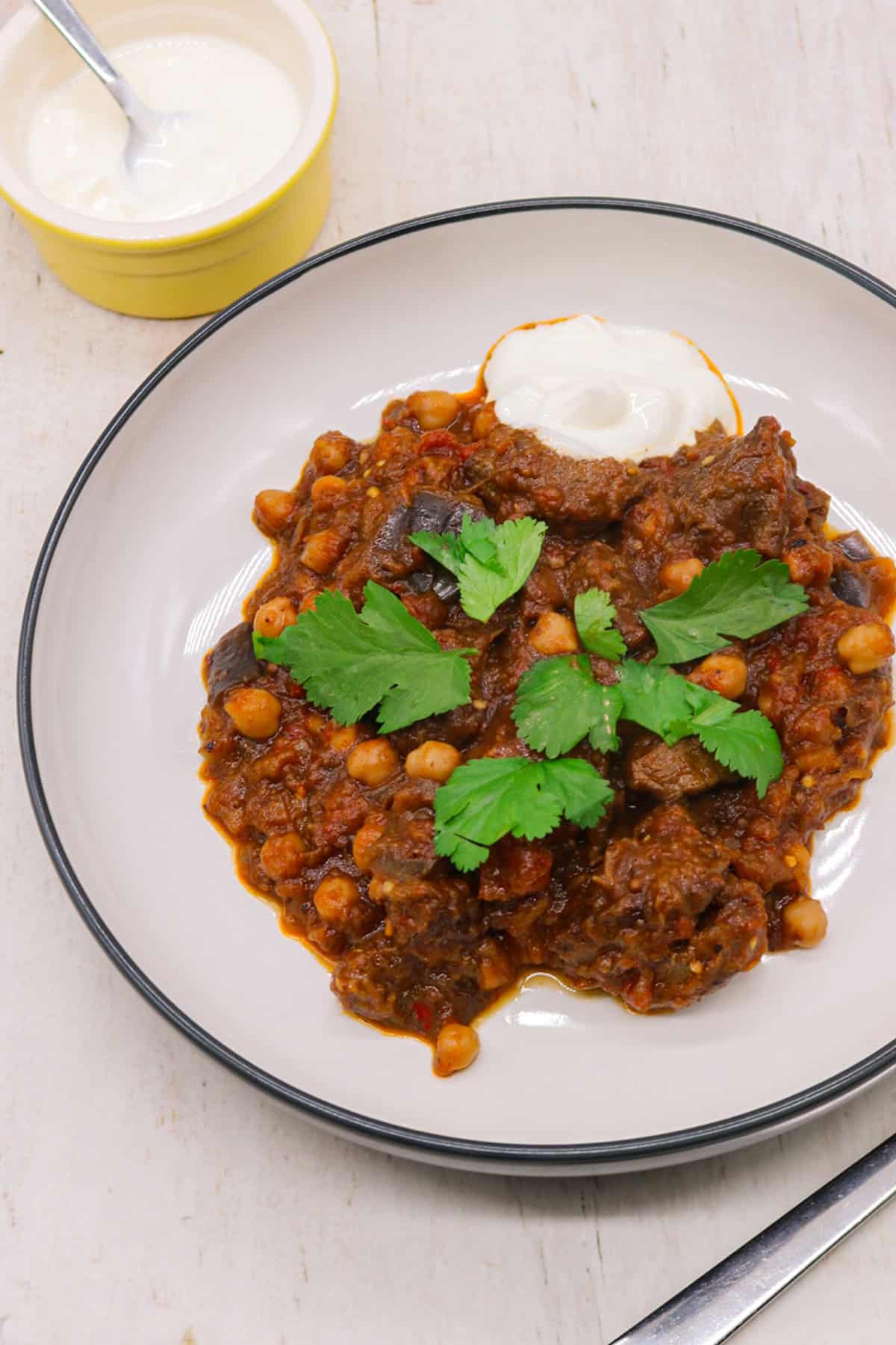 Harissa beef stew in a bowl garnished with coriander and sour cream on the side.