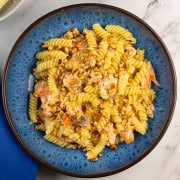 Hot smoked salmon with creamy pasta and pine nuts in a blue patterned bowl.