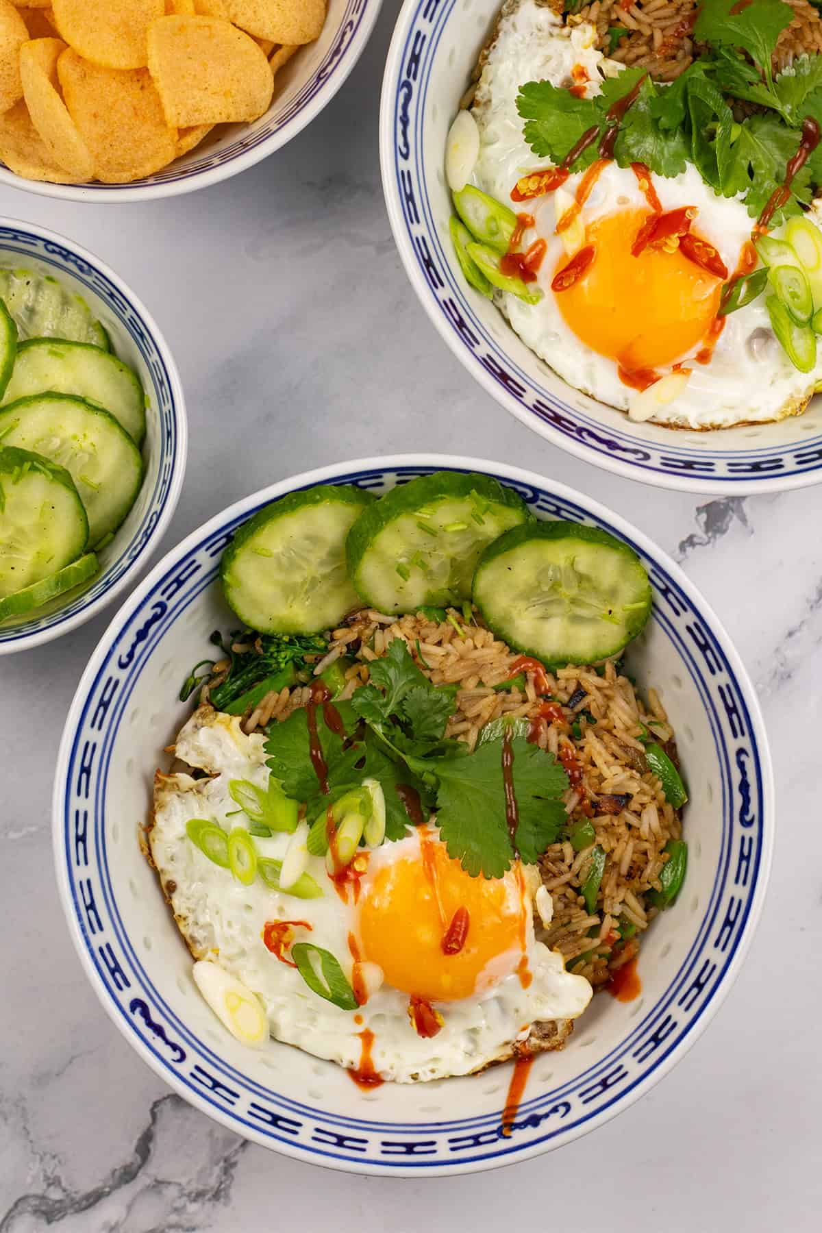 2 portions of nasi goreng in oriental bowls with bowls of cucumber pickle and Thai prawn crackers on the side.