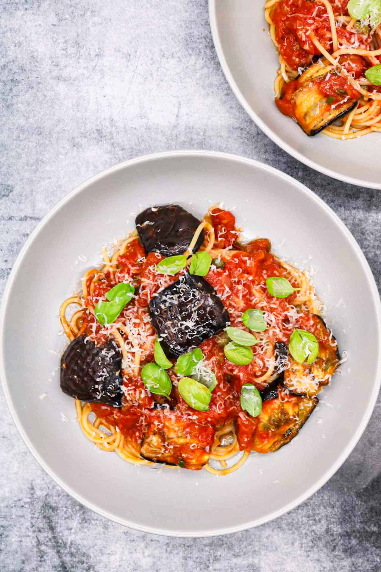 2 grey bowls of pasta all norma garnished with basil leaves and grated parmesan.