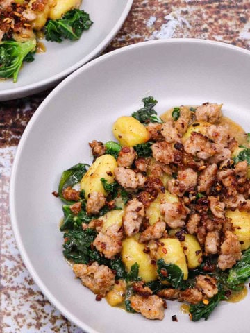 Two grey bowls of sausage, kale and gnocchi one pot.