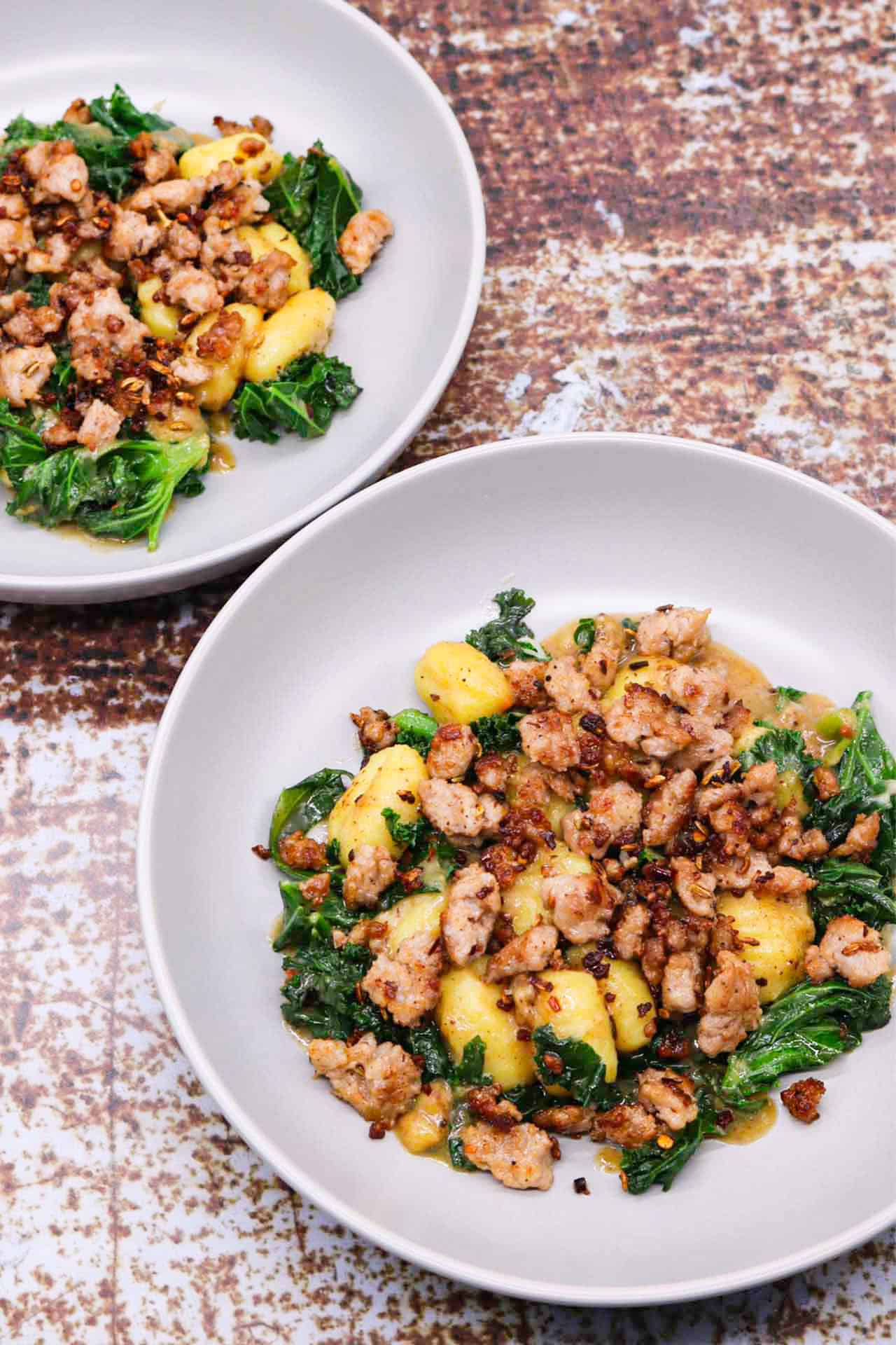 Two grey bowls of sausage, kale and gnocchi one pot.