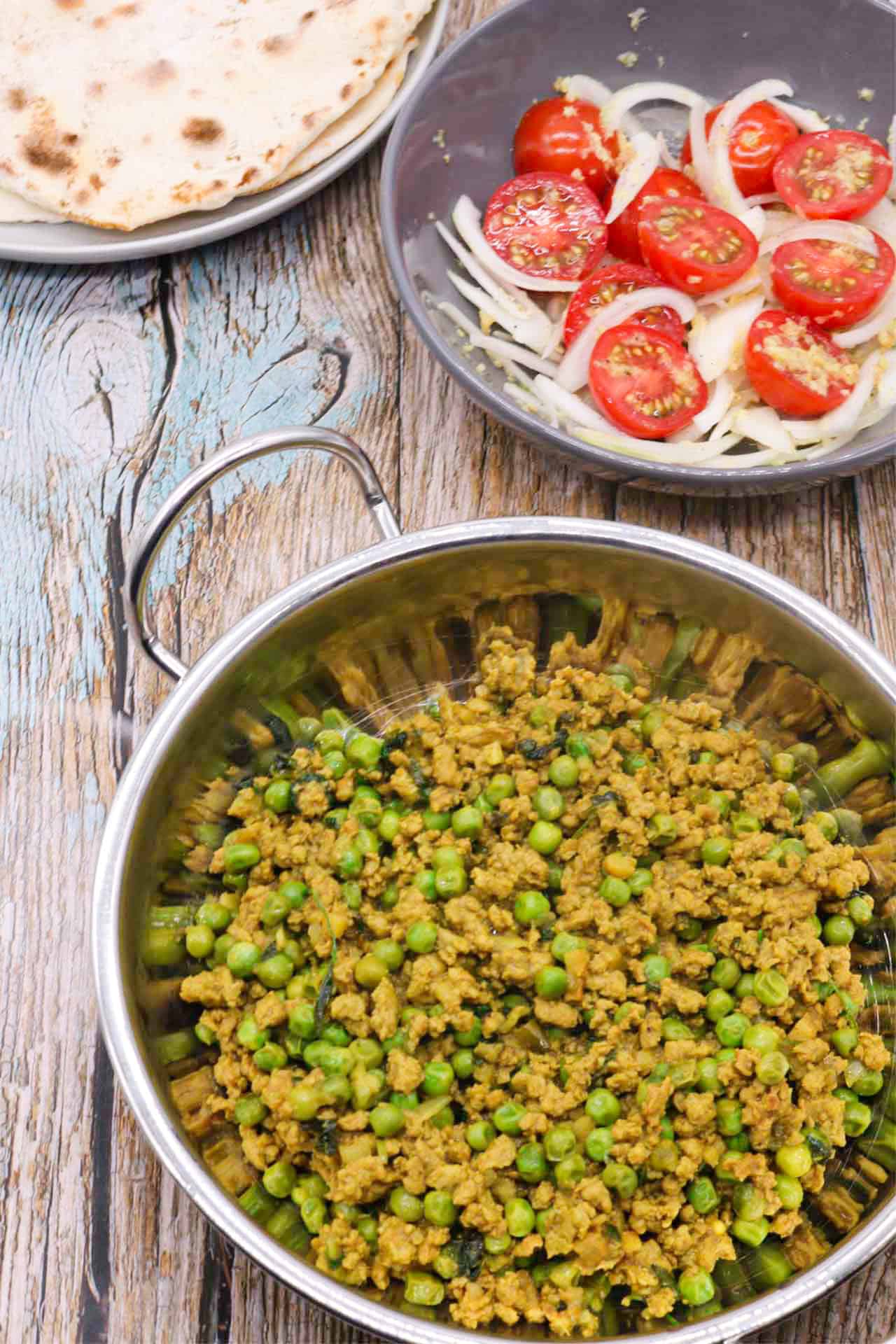 Turkey keema curry in a balti dish with a plate of naan and bowl of tomato and onion salad on the side.