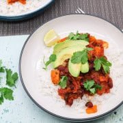 Two bowls of vegan chilli with rice, avocado, lime and coriander.