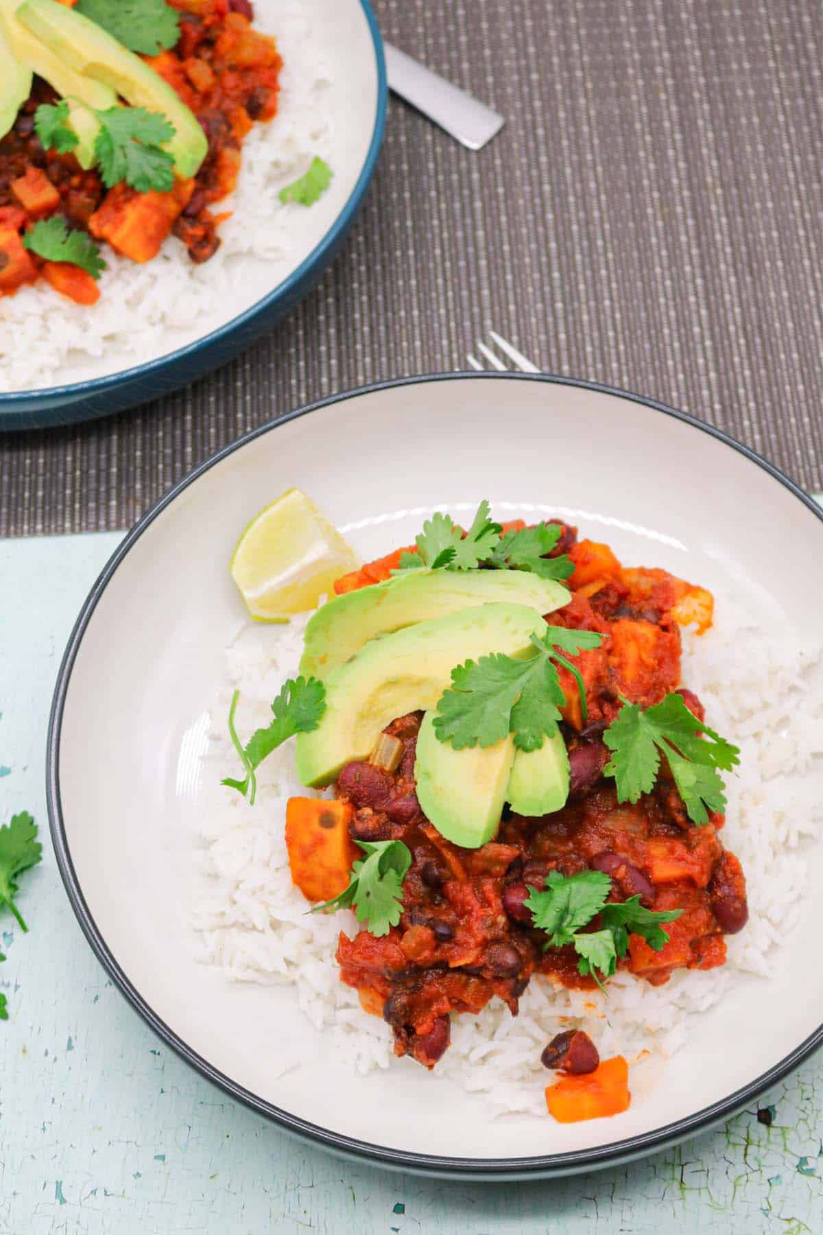 Two bowls of vegan chilli with rice, avocado, lime and coriander.