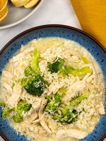 Chicken and broccoli risotto in a blue patterned bowl with a plate of sliced baguette and a mustard napkin on the side.