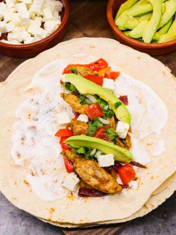 Chicken fajita in flour tortilla with avocado and cheese on wooden board