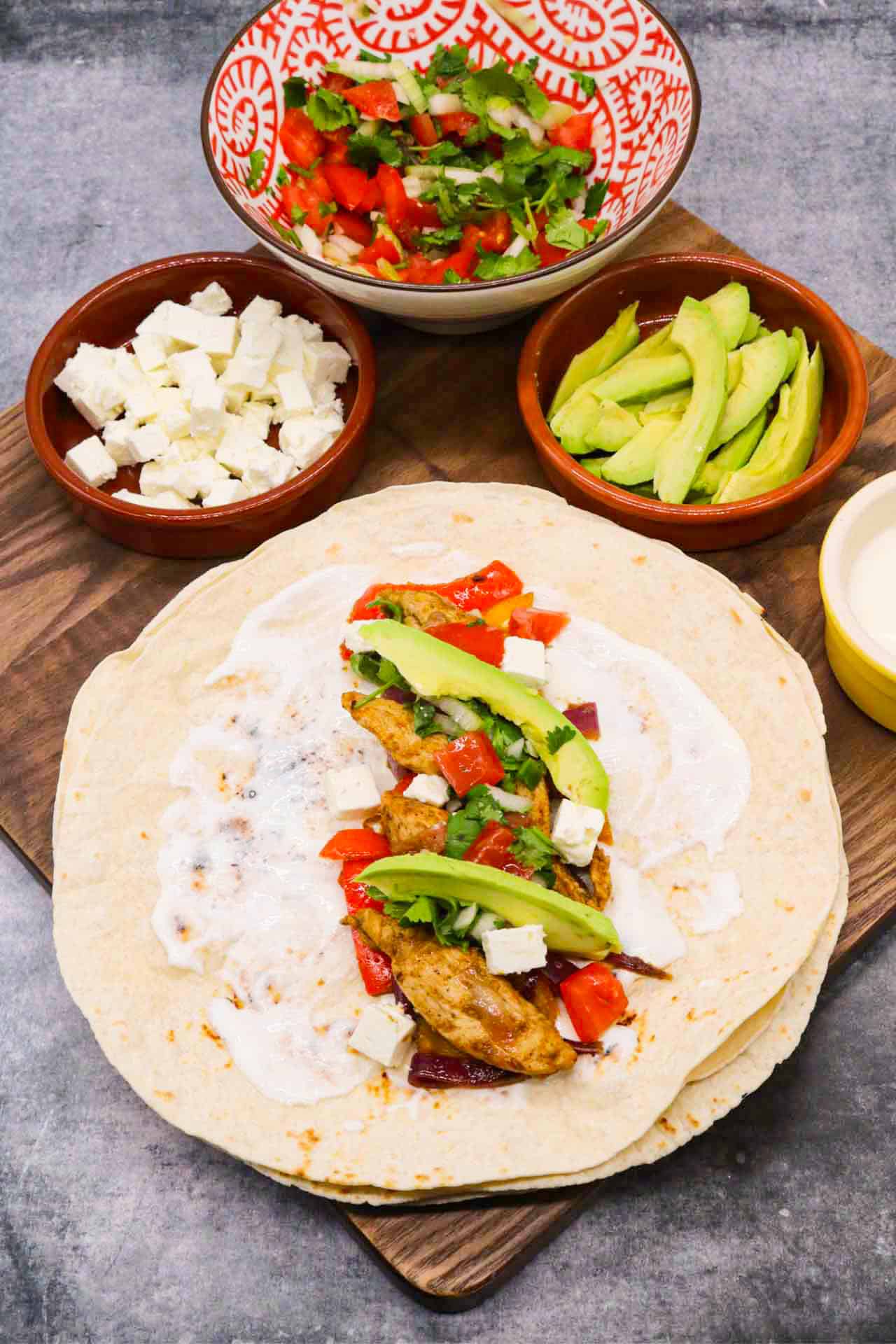 Chicken fajita in flour tortilla with avocado and cheese on wooden board