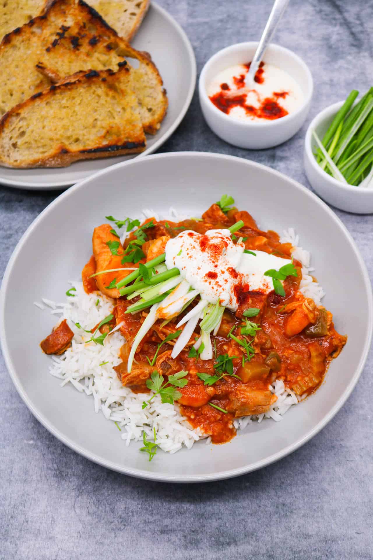 Chicken shrimp gumbo in grey bowl with rice, spring onions, soured cream and coriander