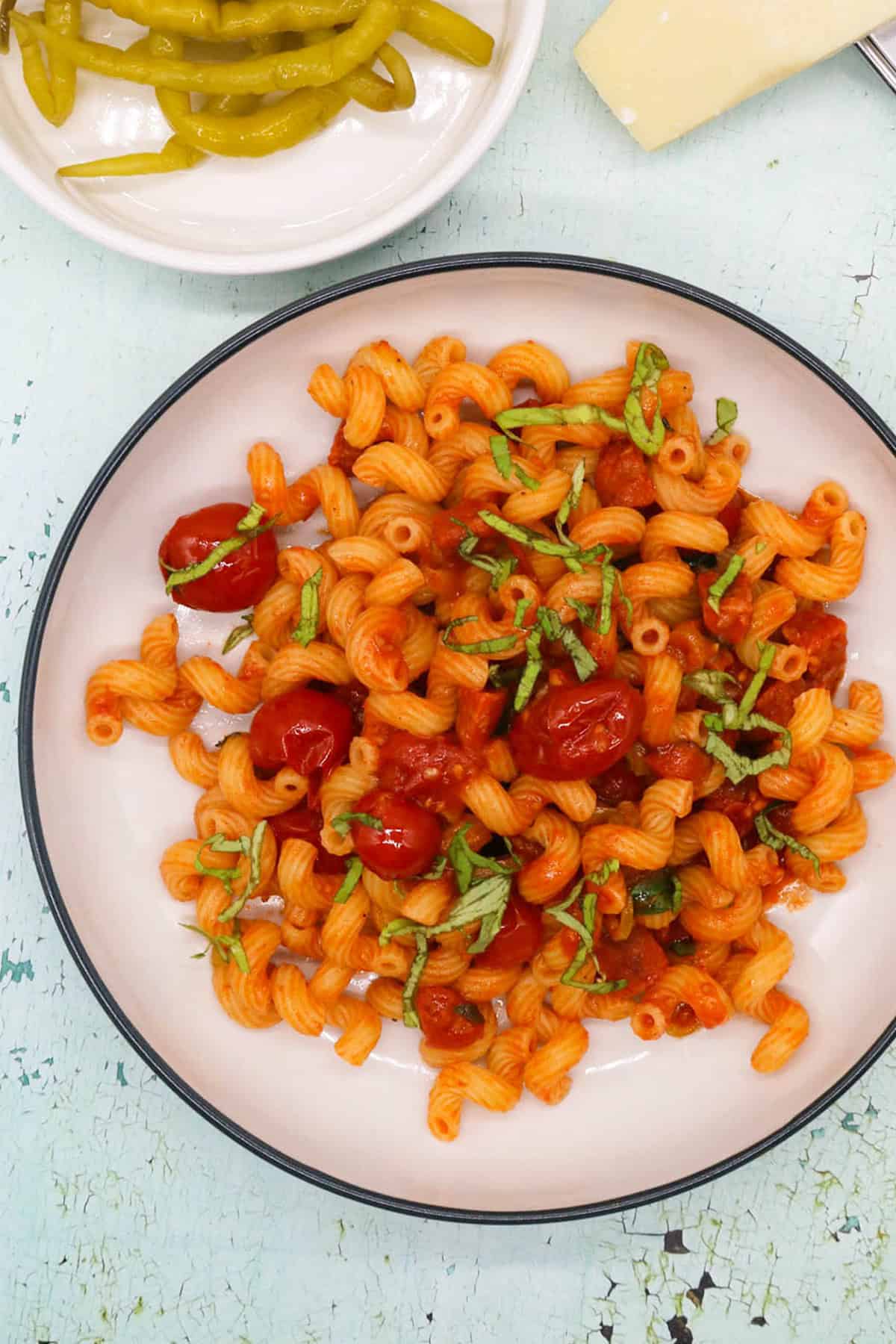 Chorizo and chilli pepper pasta in a black and cream bowl with a small dish of chilli peppers and a block of parmesan with grater on the side.