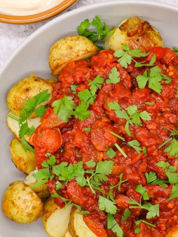 Chorizo patatas bravas in a grey serving bowl with a small dish of aioli on the side.