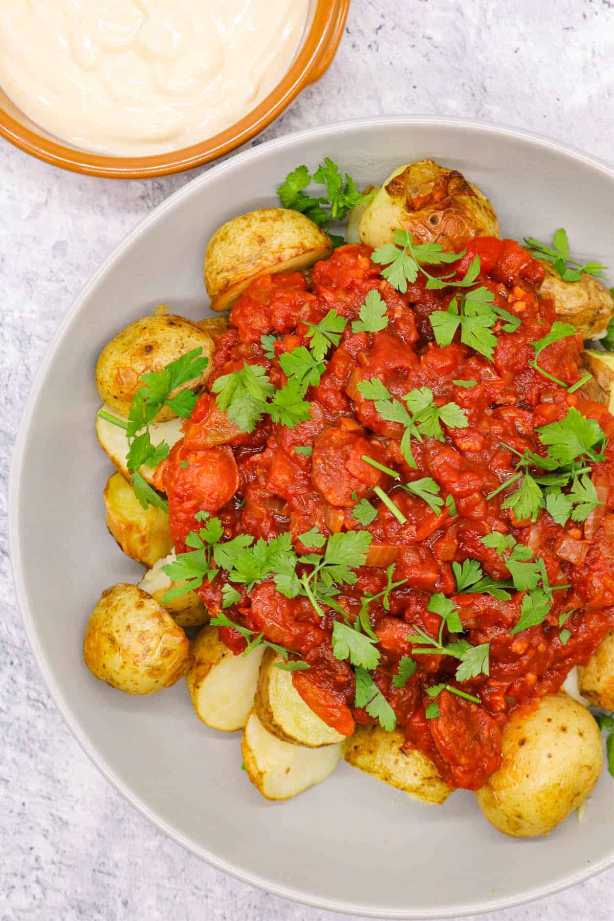 Chorizo patatas bravas in a grey serving bowl with a small dish of aioli on the side.