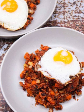 Two grey bowls with corned beef hash topped with a fried egg