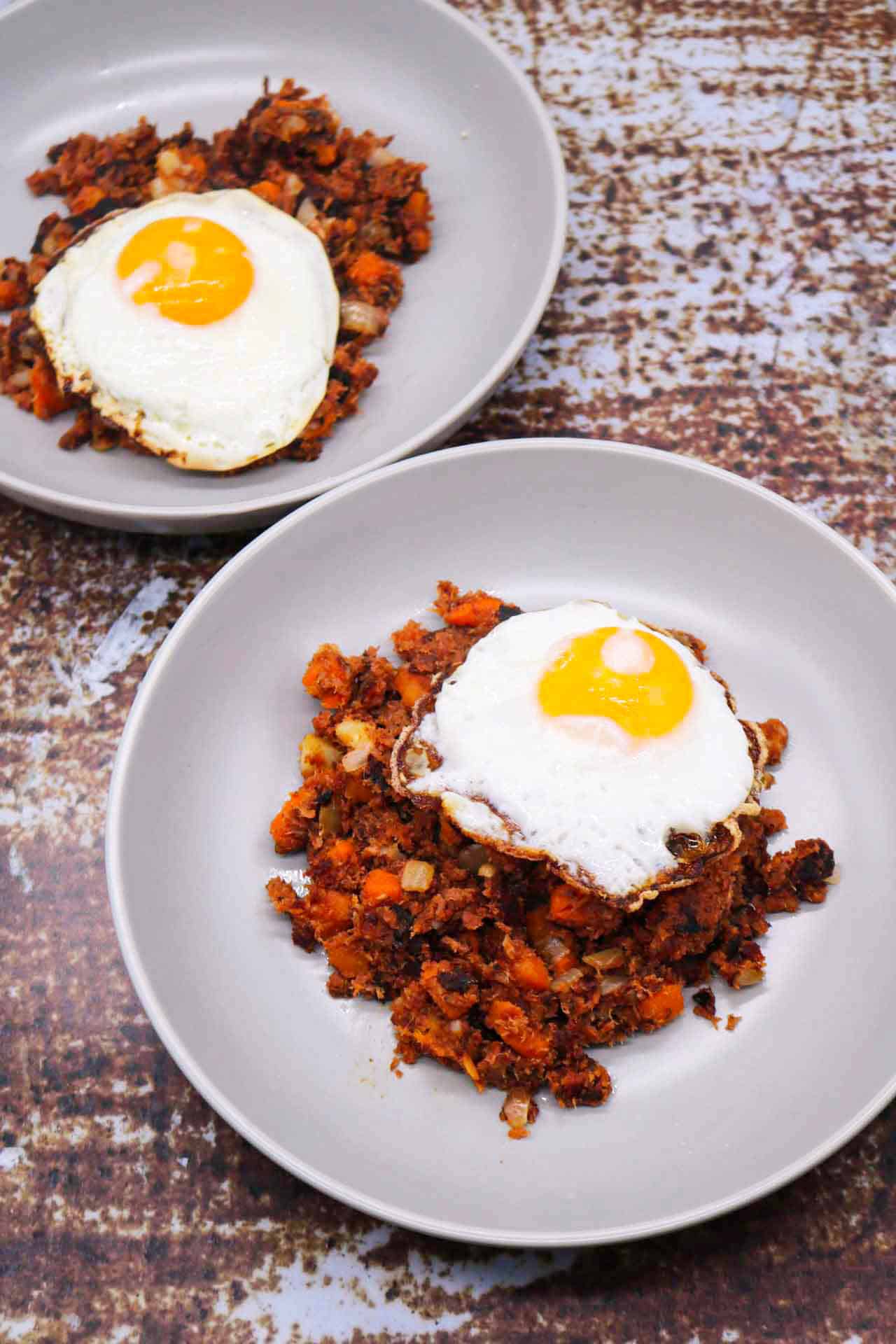 Two grey bowls with corned beef hash topped with a fried egg