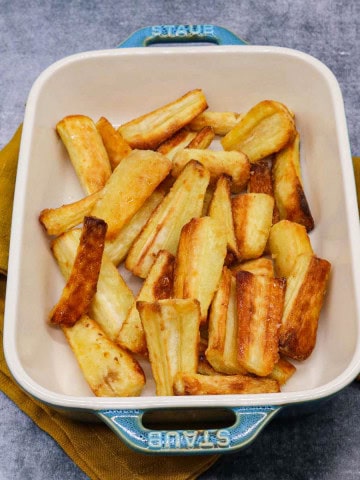 Crisp honey mustard parsnips in a rectangle serving dish with yellow napkin underneath