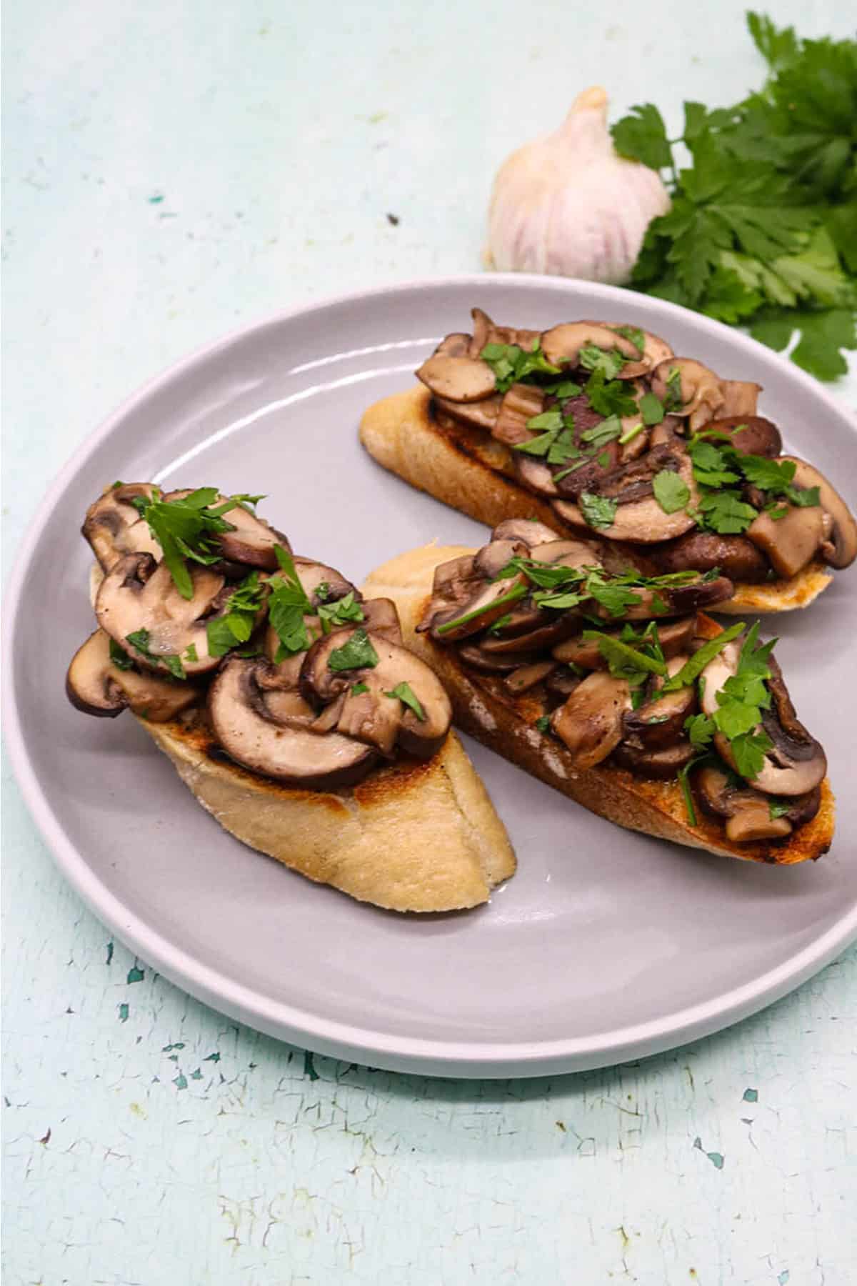 3 slices of garlic mushroom bruschetta on a grey side plate.