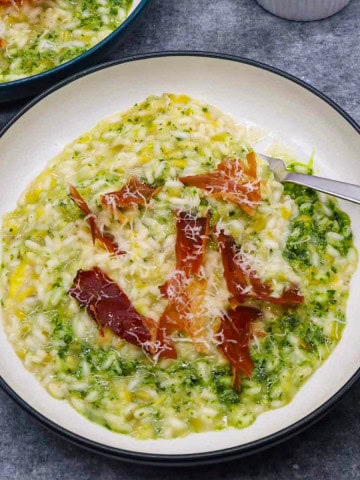 Leek risotto with kale pesto in bowl with shards of pancetta and fork