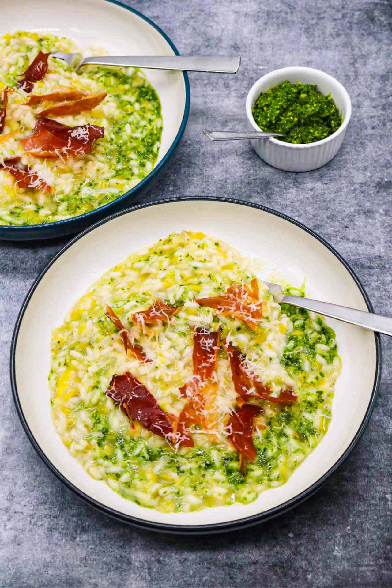 Leek risotto with kale pesto in bowl with shards of pancetta and fork