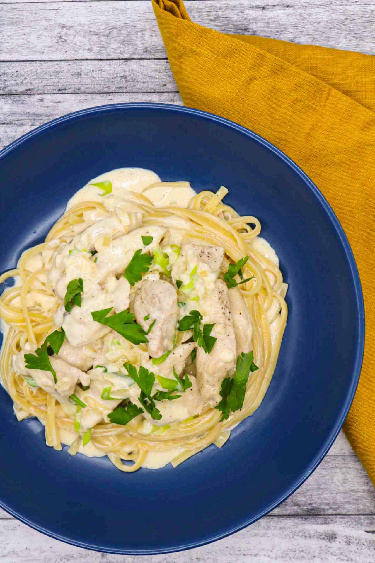 Creamy chicken linguine in blue bowl with yellow napkin at the side