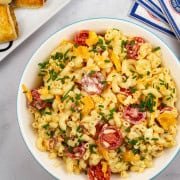 Mac 'n' cheese salad in a round serving bowl with a platter of sausage rolls and paper napkins on the side.