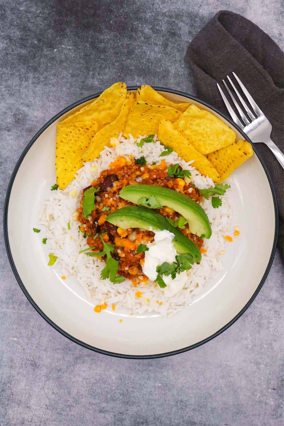 Mexican turkey chilli with rice, tortilla crisps, avocado, coriander and soured cream in bowl