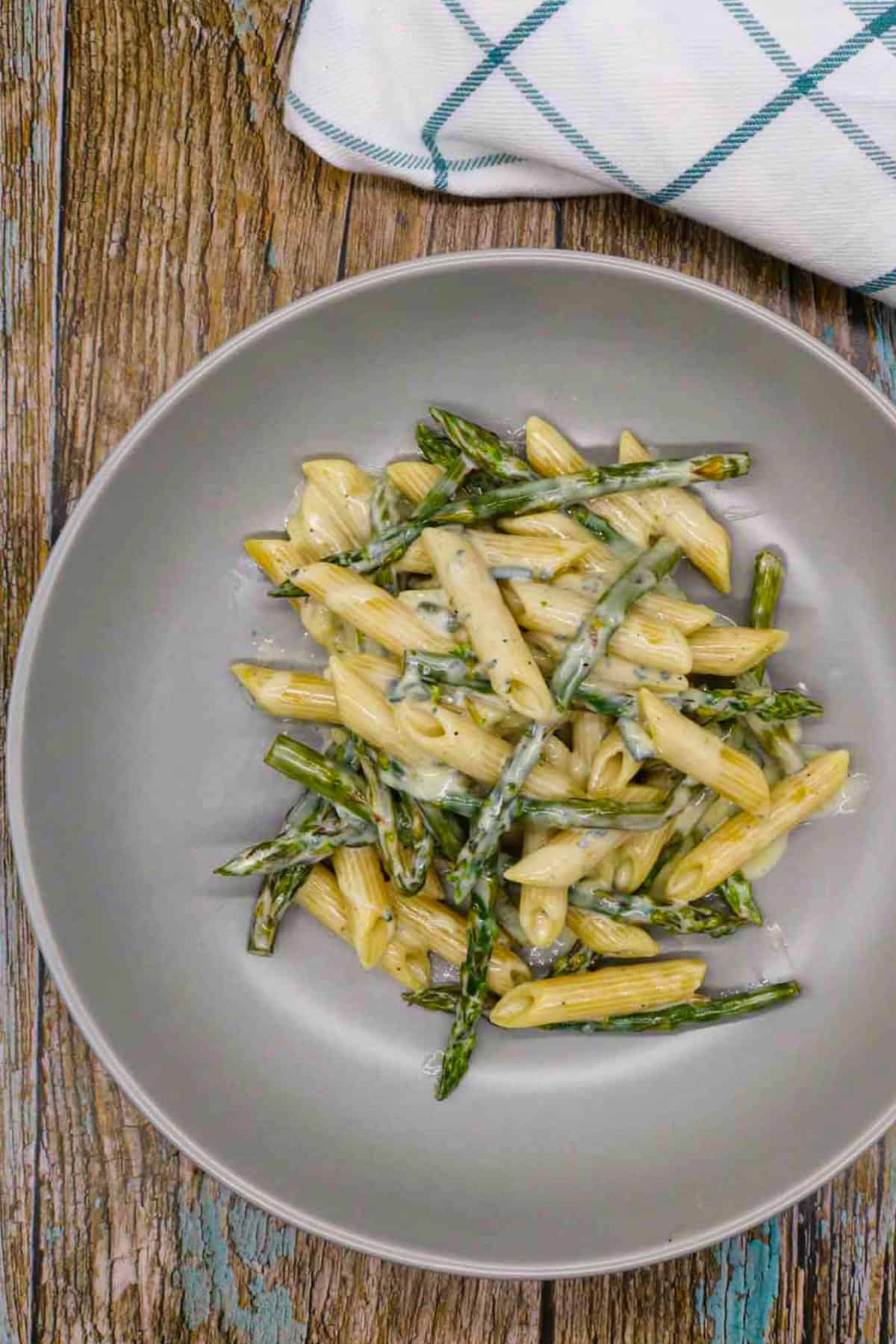 Penne with asparagus and a gorgonzola cream sauce in a grey pasta bowl with a teal and white checked towel on the side.