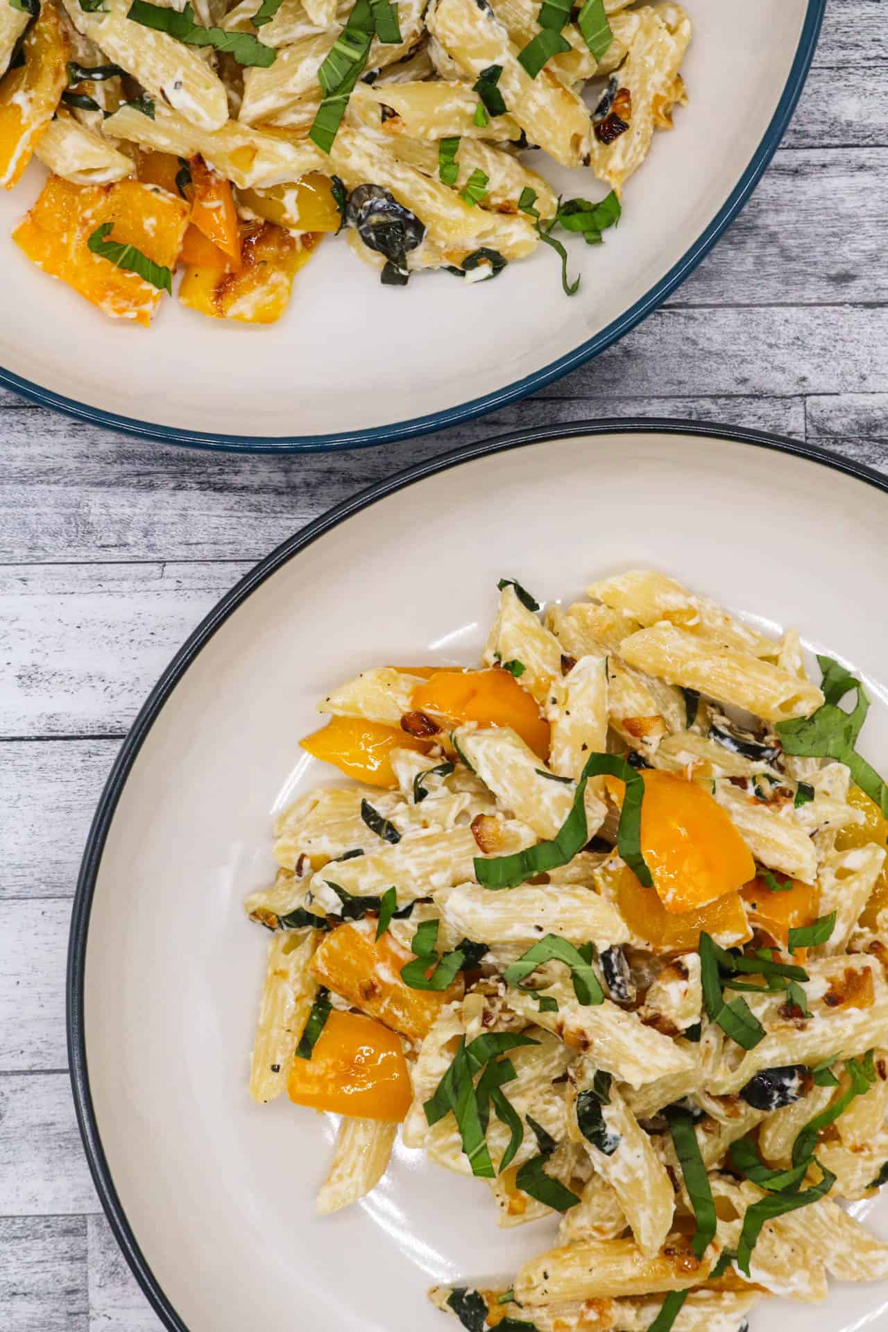 Two bowls of penne with peppers and goats cheese.