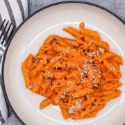 Penne alla vodka in a black and cream pasta bowl with a fork and black and white striped napkin on the side.
