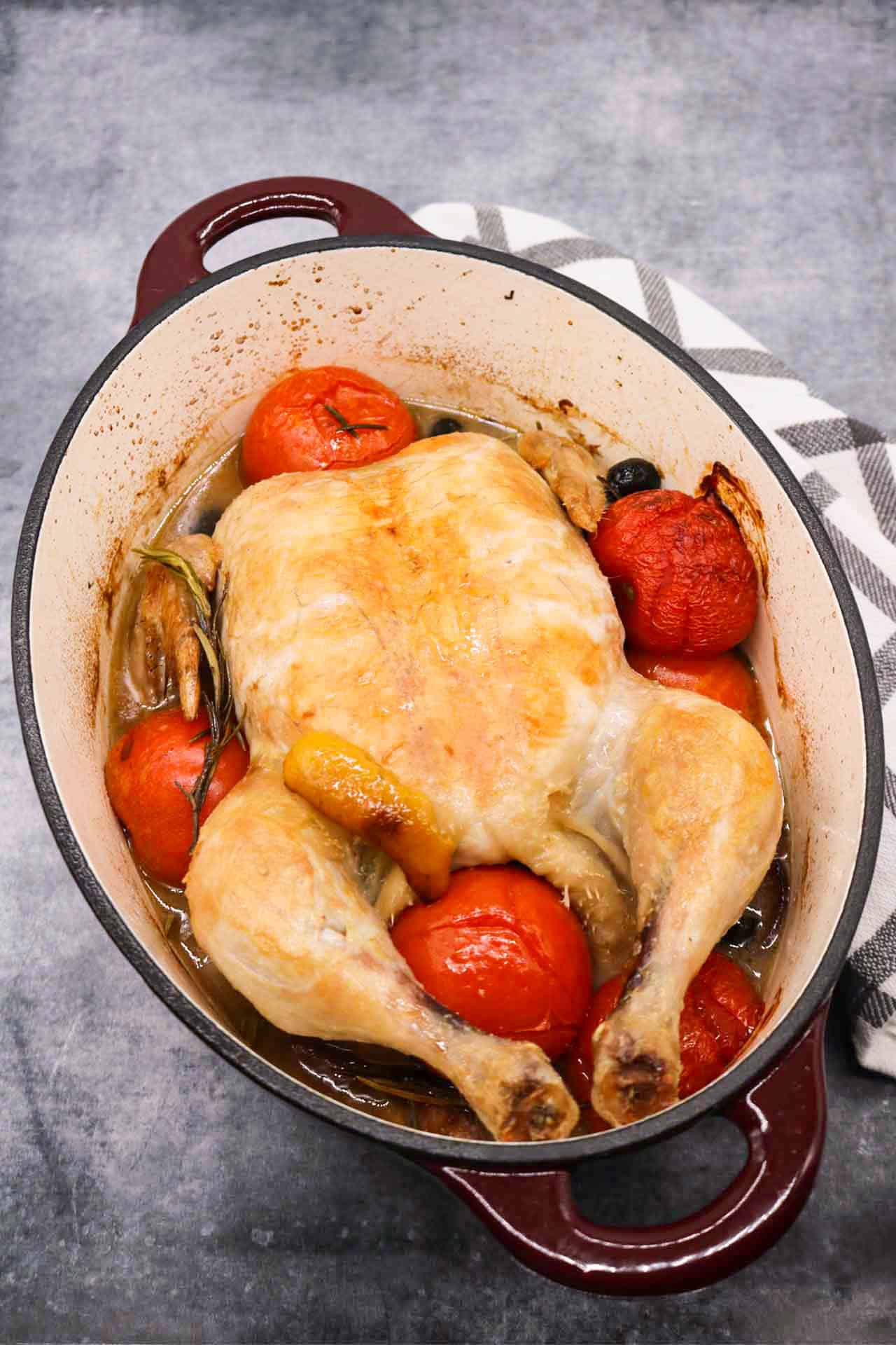 Whole chicken in oval casserole dish with tomatoes and rosemary