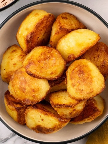 Roast potatoes in a black and cream serving bowl.