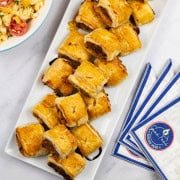 Sausage rolls on a rectangular platter with a bowl of mac 'n' cheese salad and paper napkins on the side.