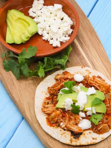 Chicken tinga on flour tortilla with avocado and cheese on wooden board