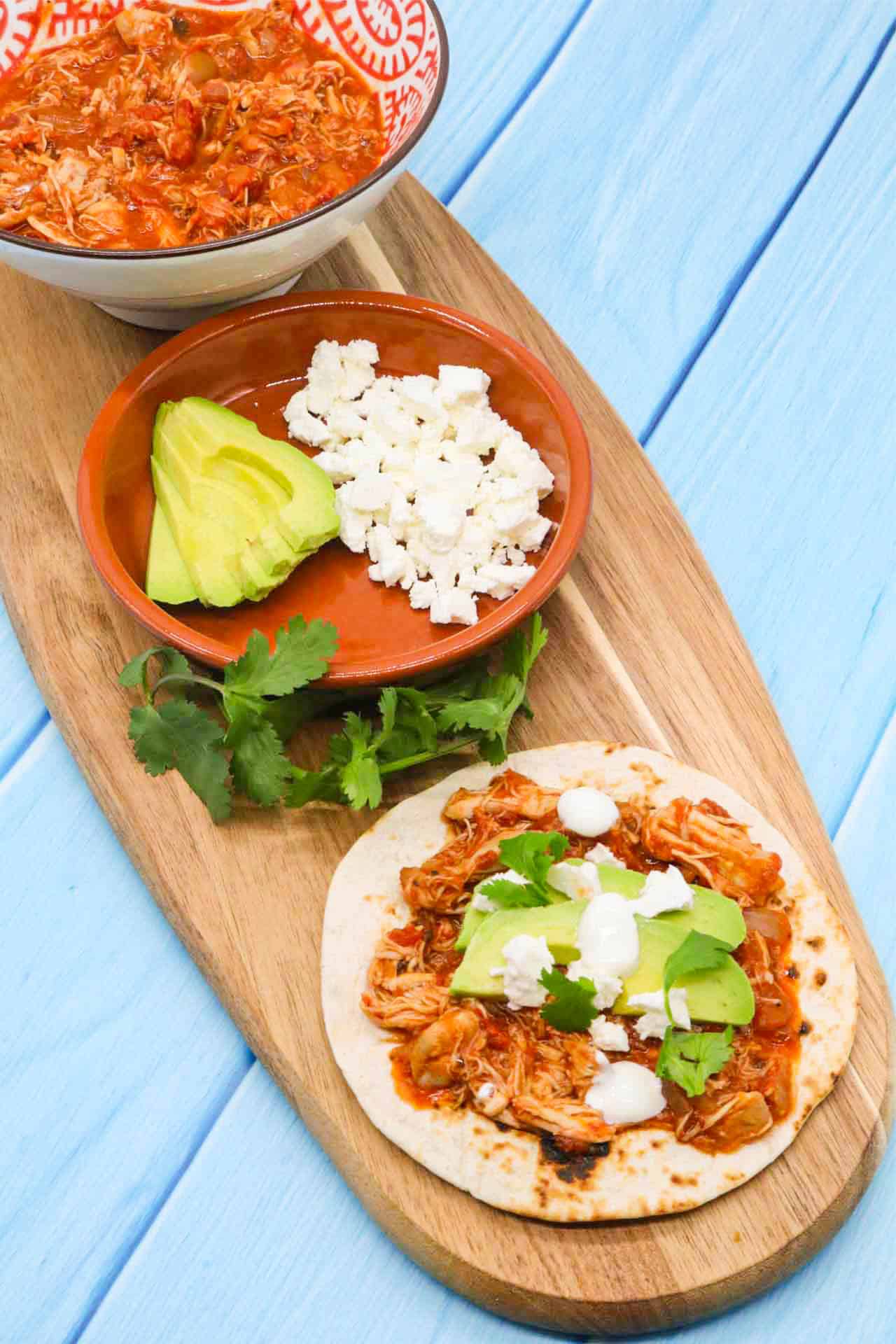Chicken tinga on flour tortilla with avocado and cheese on wooden board