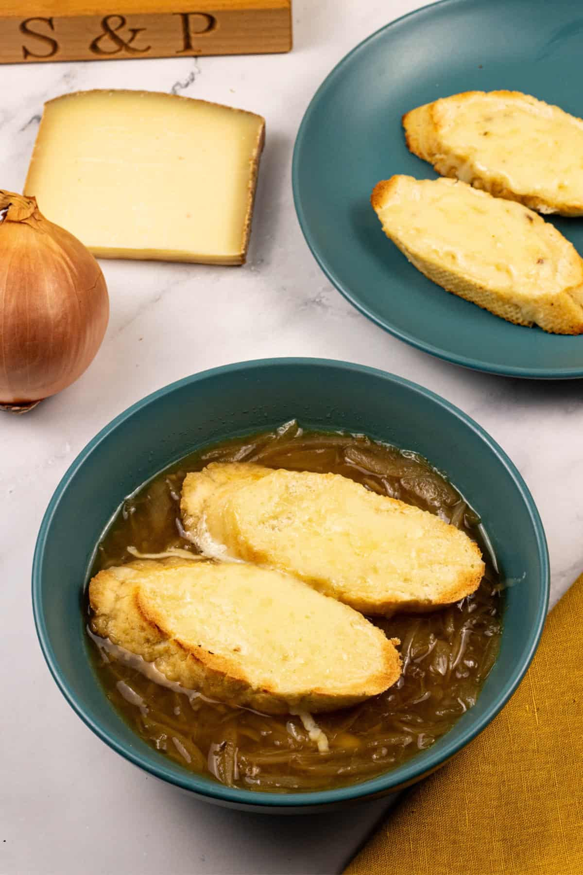 A portion of french onion soup in a teal bowl with 2 slices of baguette covered with melted cheese.
