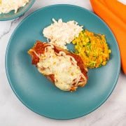Sweet potato with sausage meatball marinara, coleslaw and carrot salad on a teal dinner plate with an orange napkin on the side.