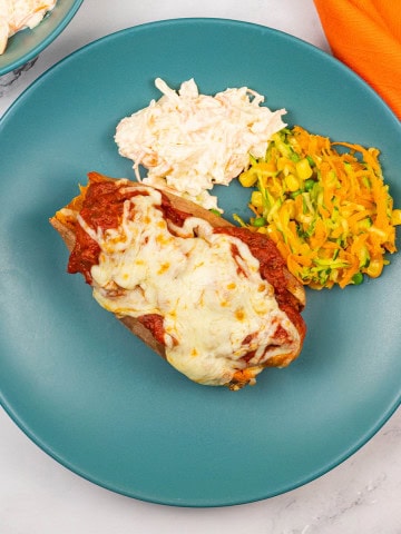 Sweet potato with sausage meatball marinara, coleslaw and carrot salad on a teal dinner plate with an orange napkin on the side.